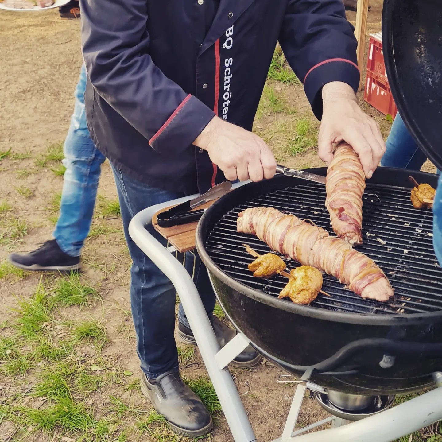 Grillmeister wendet Bacon-Rollen auf einem Kugelgrill bei einem Fest