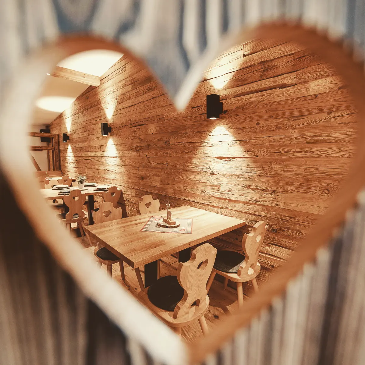 Blick durch ein herzförmiges Holzelement in die warm beleuchtete Alm